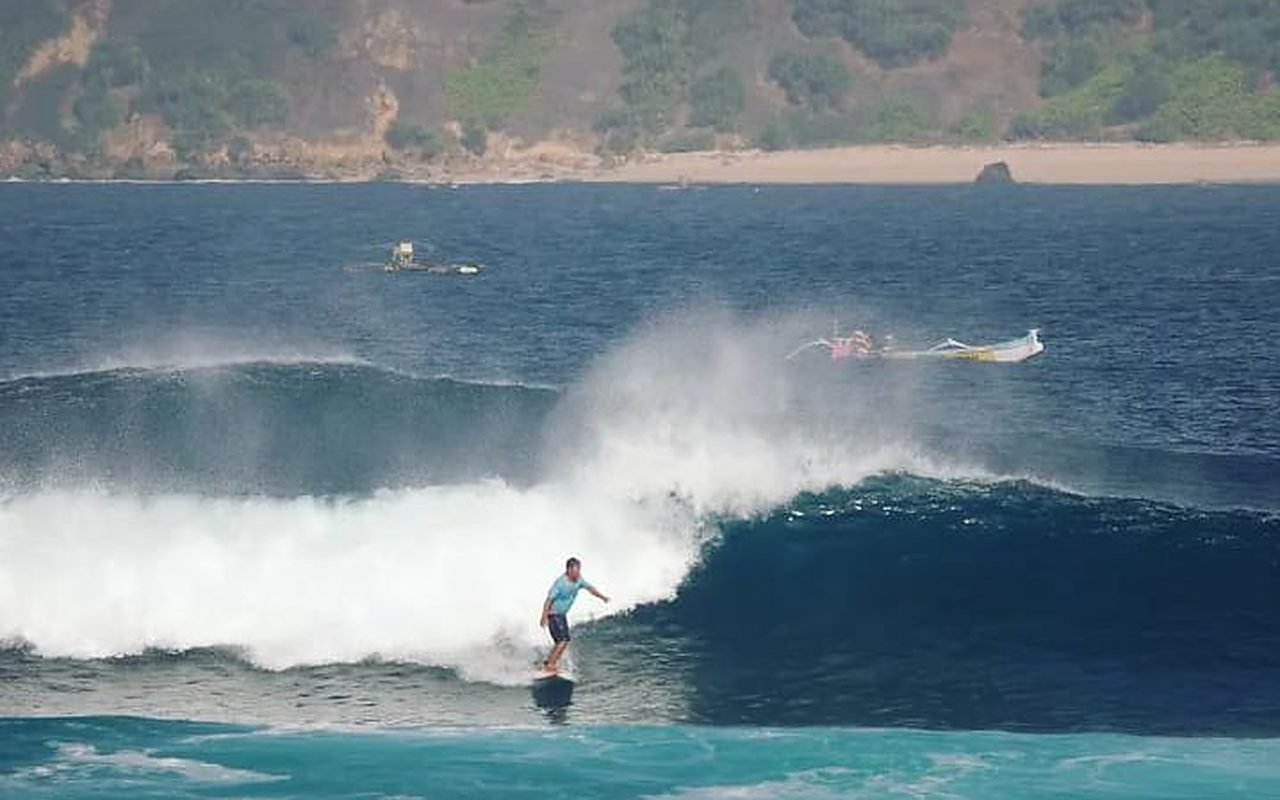 A surfer dropping into a turquoise wall on the reef at Ekas